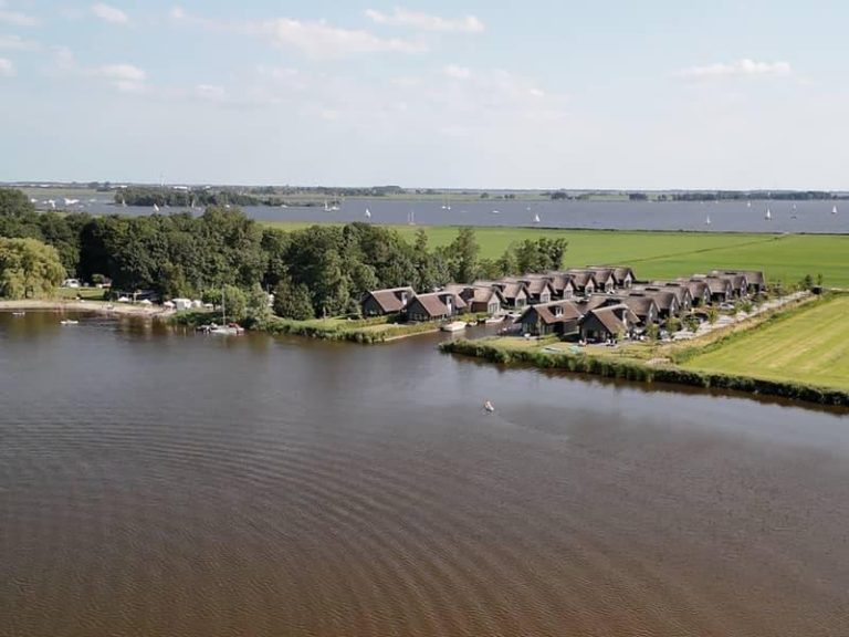 Uitzicht op een vakantiehuis in Friesland met boot aangelegd aan het water, omgeven door natuur en riet